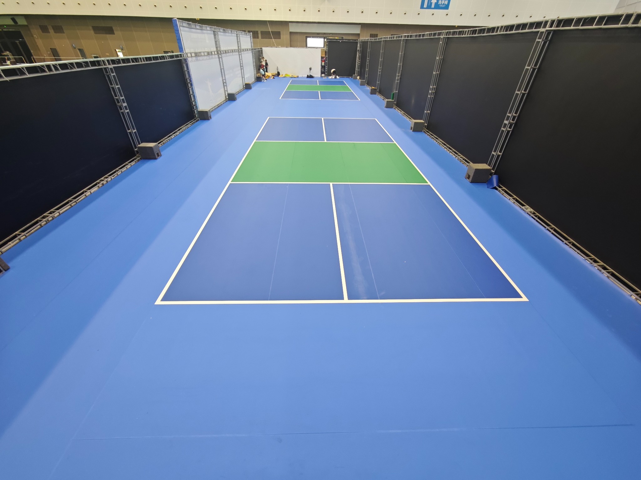 Long indoor event hall with two blue and green pickleball courts