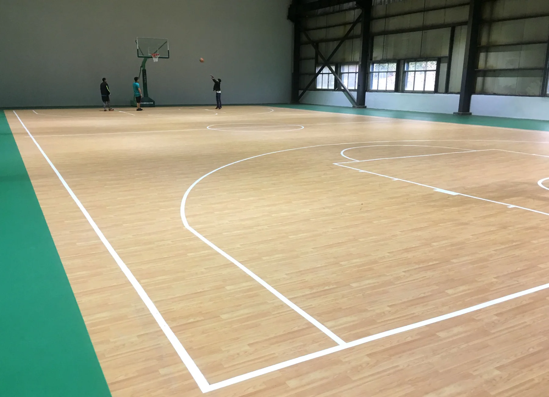Indoor basketball court with light wood-pattern sports flooring and green perimeter