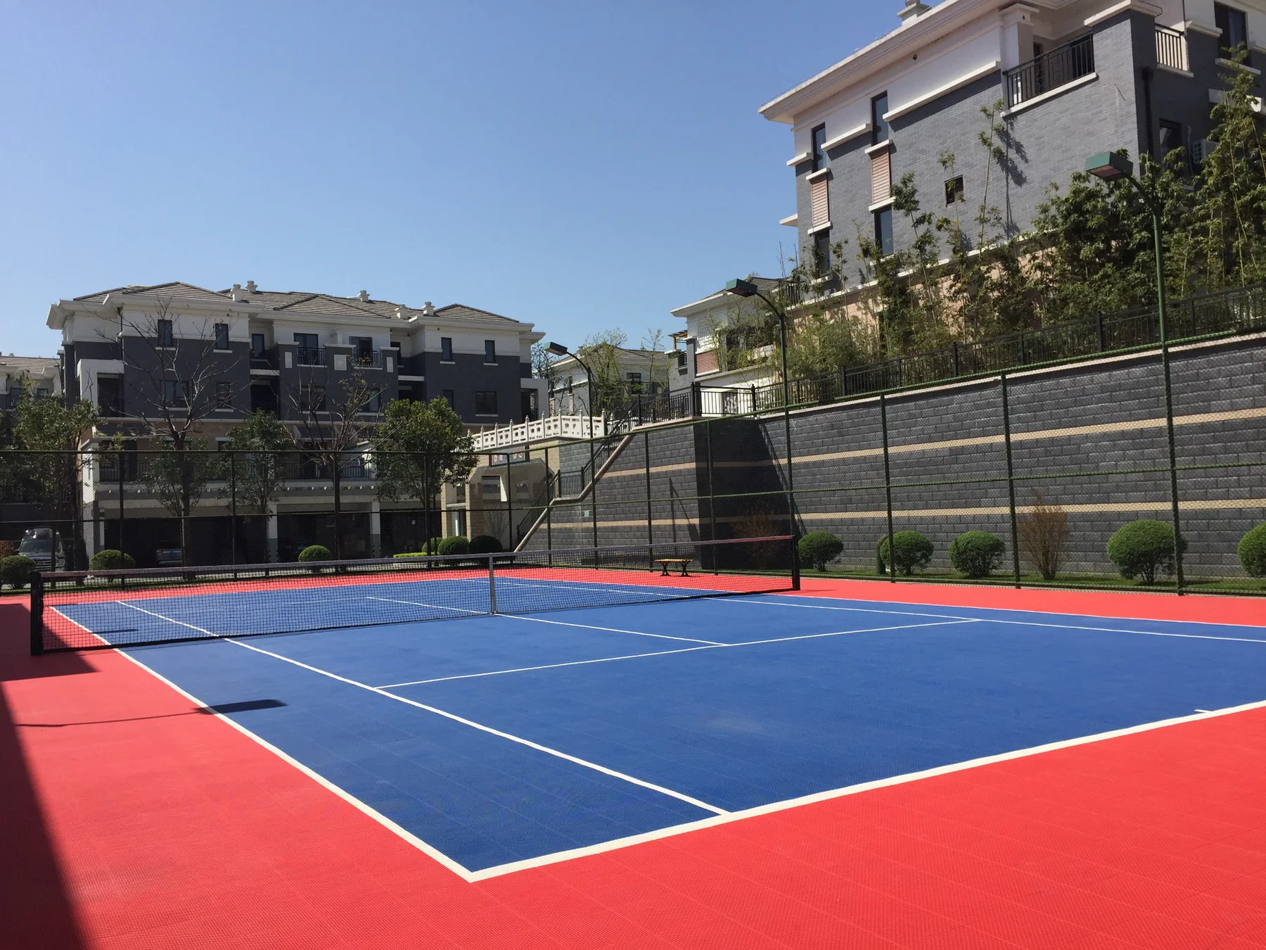 Private blue and red outdoor tennis court beside residential buildings