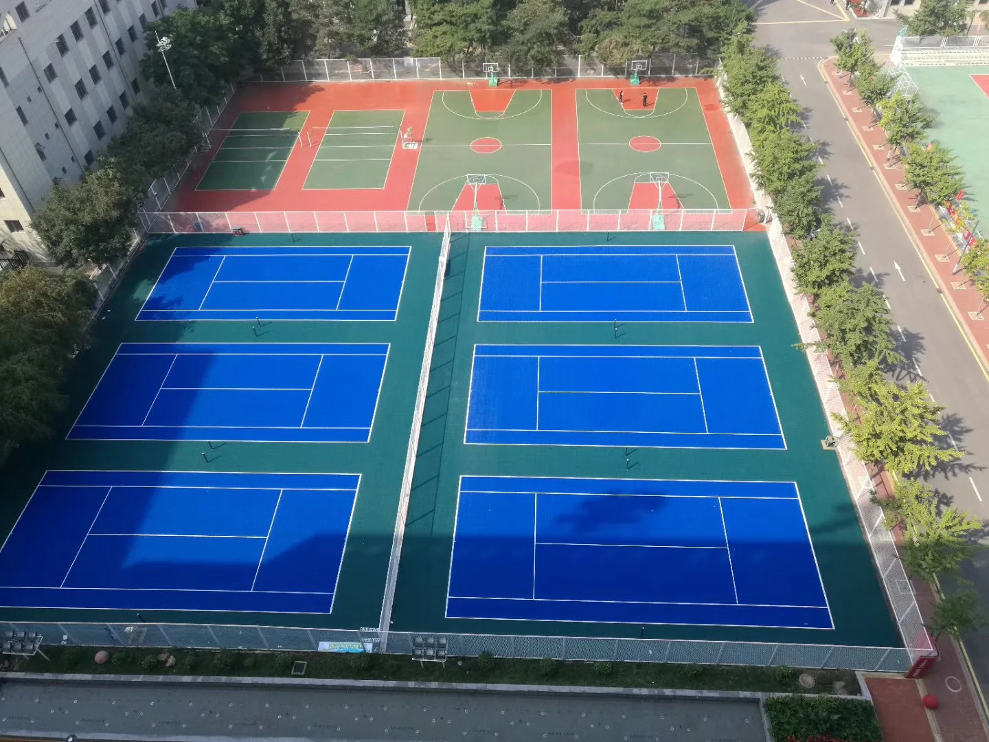 Aerial view of six blue outdoor tennis courts beside basketball courts