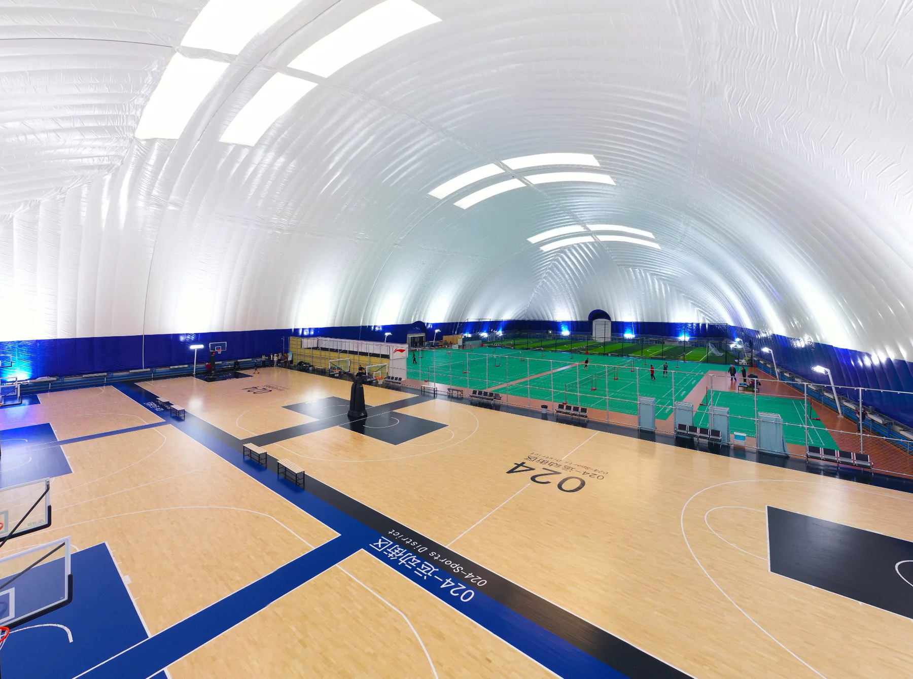 Large clear-span air dome interior containing basketball and badminton courts
