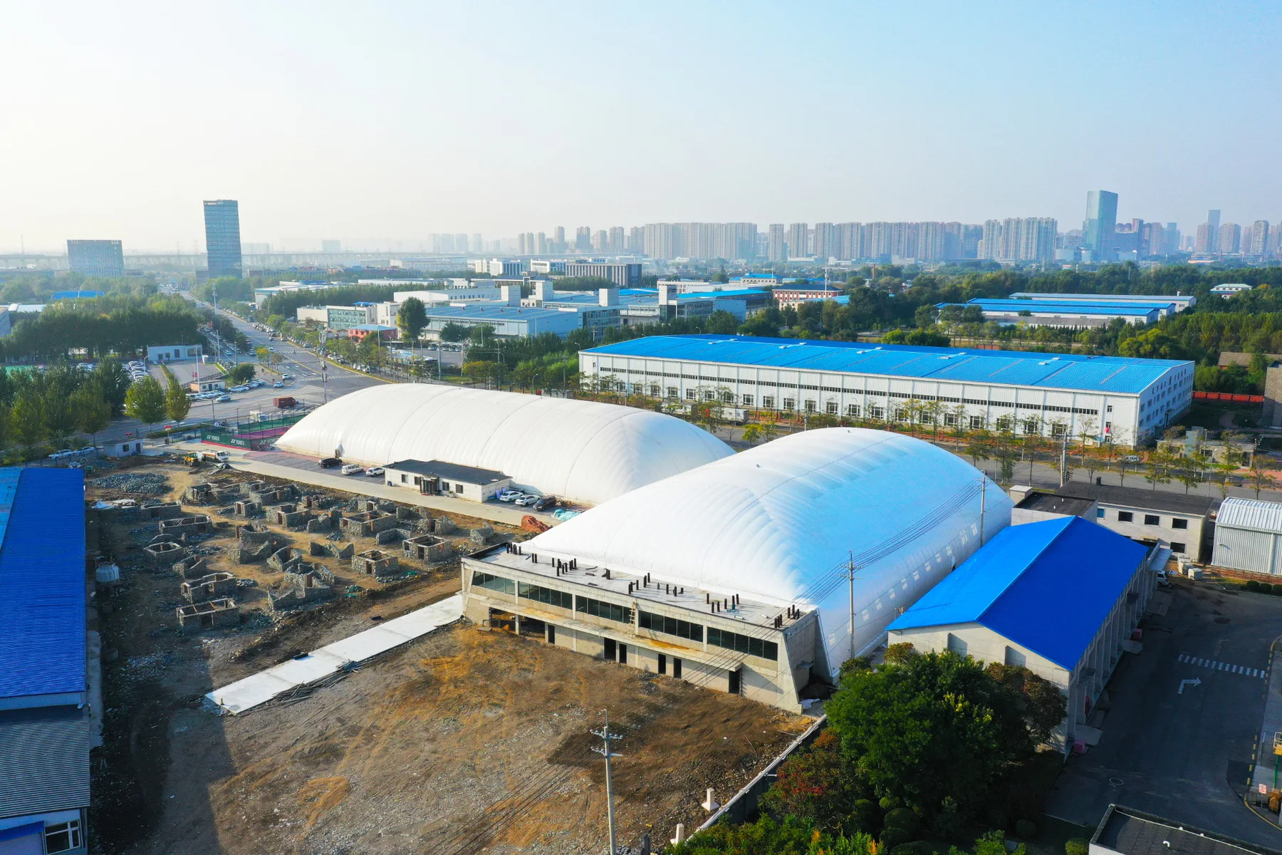 Aerial view of two large air-supported sports domes beside an industrial facility