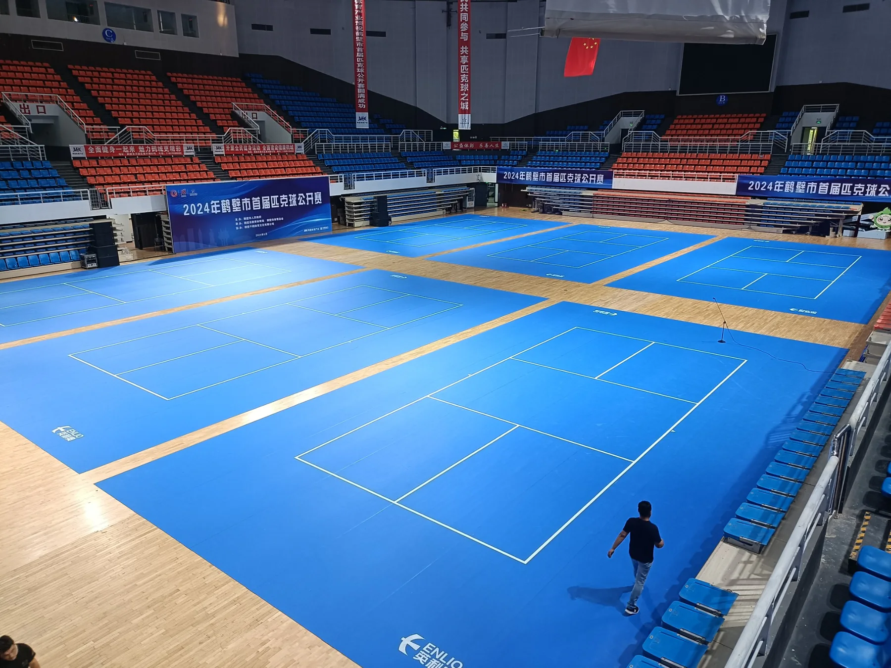 Wide indoor arena view of multiple blue pickleball courts